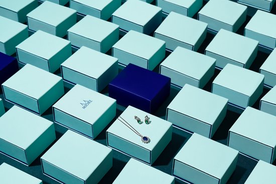 Een halsketting met blauwe en groene steentjes, en bijpassende oorbellen, liggen op een open geschenkdoos.