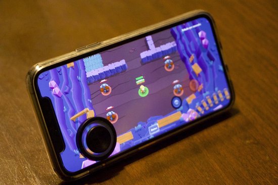 Smartphone met een spel op het scherm en een zwarte joystick-accessoire bevestigd.