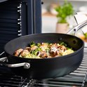 Zwarte hapjespan met gehaktballetjes, broccoli en pasta, op een kookplaat.