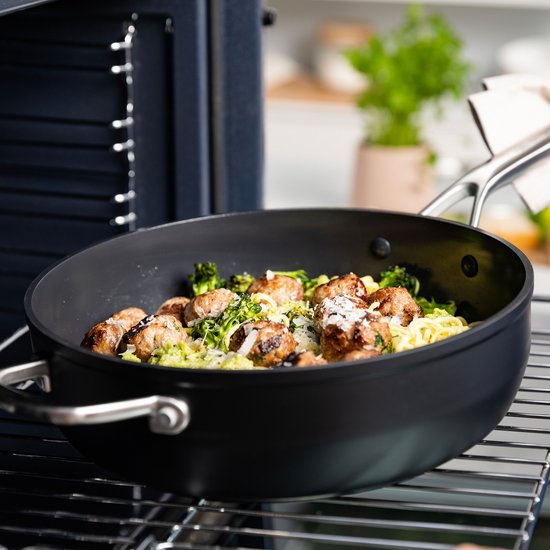 Zwarte hapjespan met gehaktballetjes, broccoli en pasta, op een kookplaat.