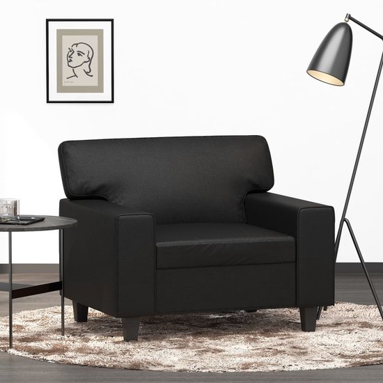 Zwarte fauteuil met armleuningen, op een zachte ronde mat, naast een bijzettafel.