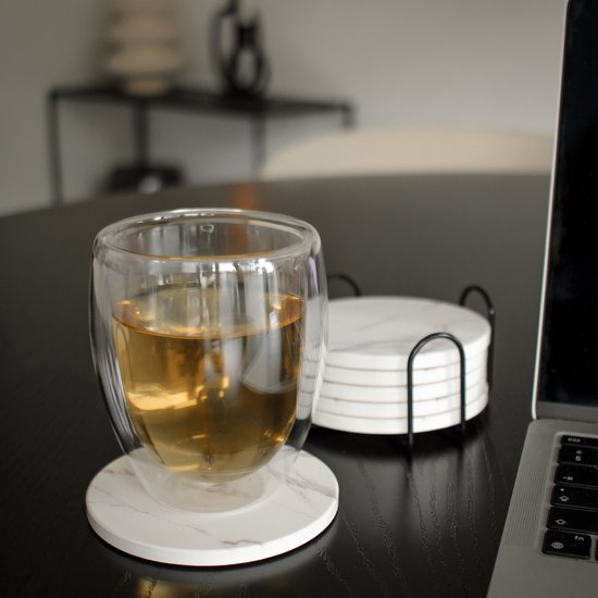 Un sous-verre rond aspect marbre sous un verre de boisson, à côté d'un ordinateur portable sur une table sombre.