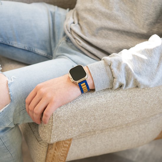 Model draagt een Apple Watch met een blauw en goudkleurig metalen bandje.
