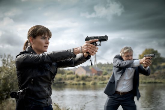 Vrouw met leren jas en man met pak richten hun wapens.