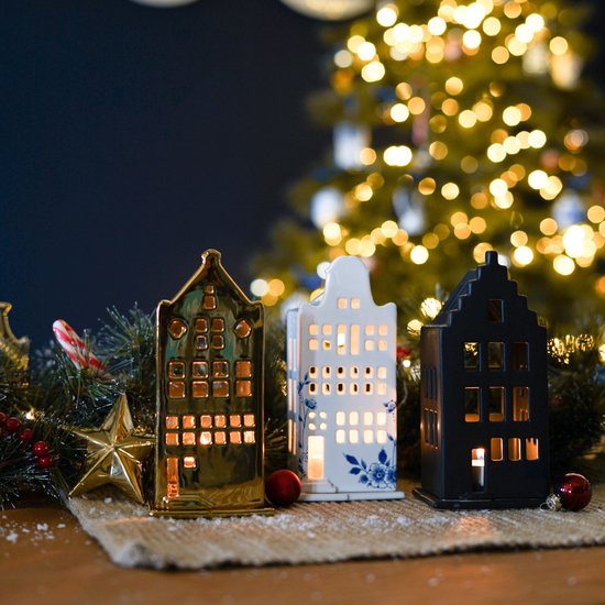 Drie waxinelichthouders in huisvorm: goud, wit met blauw en zwart, voor een kerstboom.