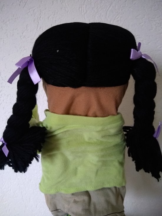 Achterkant van een pop met zwarte vlechten, paarse strikjes, groen shirt en spijkerrokje.