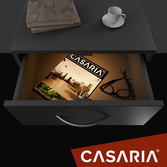 Open lade van een grijs nachtkastje met een Casaria tijdschrift en een bril erin. Bovenop de lade liggen boeken en een kopje.
