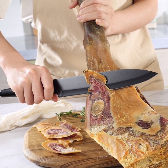 Iemand snijdt met een zwart Paudin mes een stuk ham op een houten snijplank.