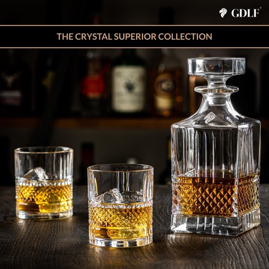 Een kristallen whiskykaraf en twee glazen gevuld met amberkleurige drank, met ijsblokjes op een donkere houten tafel.