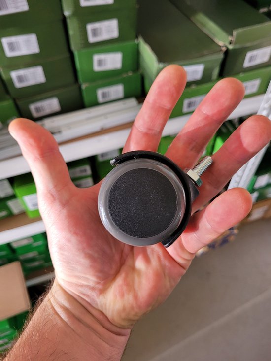 Grijs meubilair wiel met zwarte remhendel en schroefdraad, in een hand.