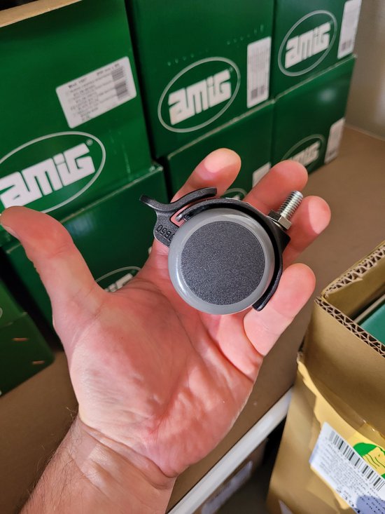 Grijs meubilair wiel met zwarte remhendel en schroefdraad, in een hand.