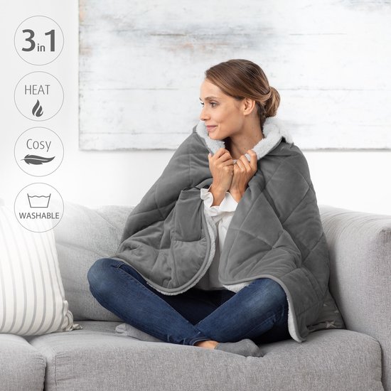Vrouw zittend op een bank, draagt een grijze, verwarmde deken, met iconen voor 3-in-1, warm, cosy, wasbaar.