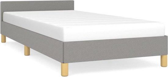 Grijs stoffen bedframe met houten poten en wit matras.