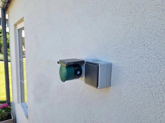 Een witte buitenstekkerdoos met een grijze behuizing en een groene ronde afdekking.