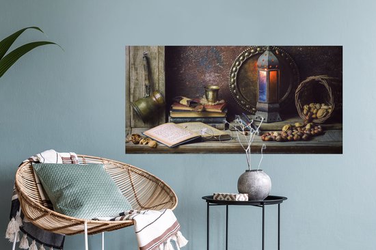 Un livre ouvert avec des lunettes, une pile de livres, des noix, une lanterne et une bouilloire en cuivre sur une étagère en bois dans une pièce.