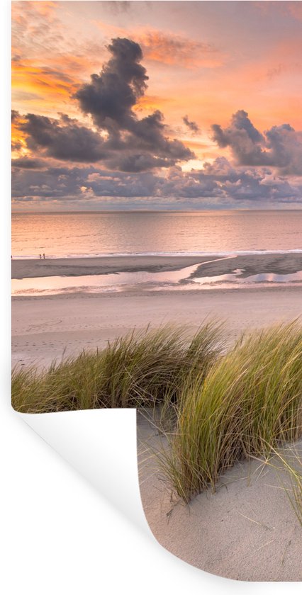 Zonsondergang met wolken boven de zee en duinen met gras, een deel van de muursticker is opgerold.