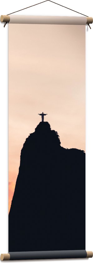 WallClassics - Textielposter - Silhouet van Jezusbeeld op berg met Zonsondergang - 30x90 cm Foto op Textiel