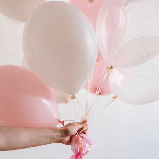 Hand houdt een bos pastelroze en witte ballonnen vast, met satijnen linten.