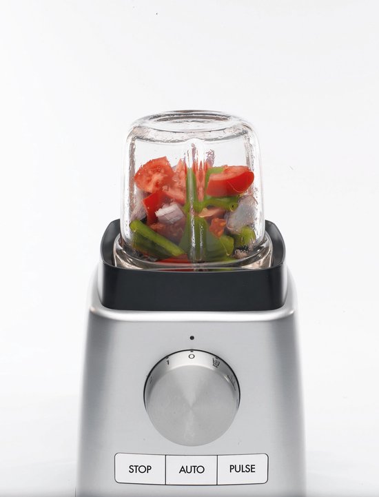 Zilverkleurige blender met glazen beker gevuld met stukjes tomaat en groene groenten.