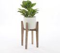 Groene kunstplant in een lichte ronde pot, geplaatst op een houten standaard.