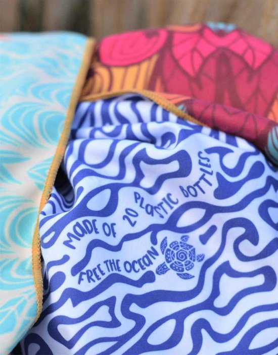 Close-up van een strandlaken met een blauwe golvenprint, met de tekst 'Made of 20 plastic bottles' en een schildpadlogo.