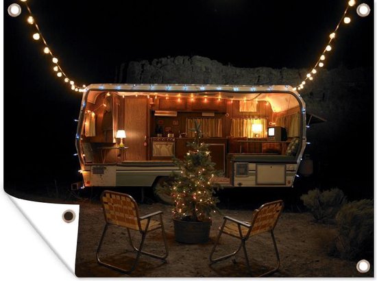 Een camper in de nacht met een kerstboom en stoelen, versierd met lichtjes.