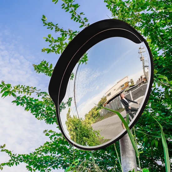Une femme en costume fait du vélo, reflétée dans un miroir convexe à bord noir, entourée de verdure.