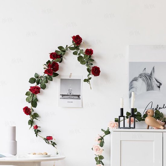Een slinger van rode rozen hangt aan een muur, met een foto en decoraties ernaast.