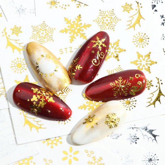 Verschillende kunstnagels met gouden winterse motieven, zoals sneeuwvlokken en tekst.