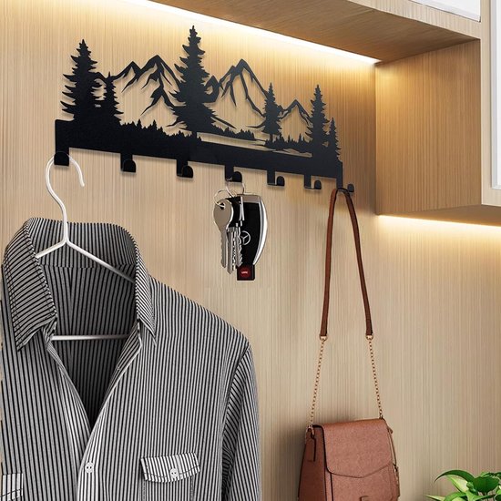 Zwart metalen sleutelhanger met bergen en bomen silhouet, hangt aan een muur, met een gestreept shirt en een tas eraan.