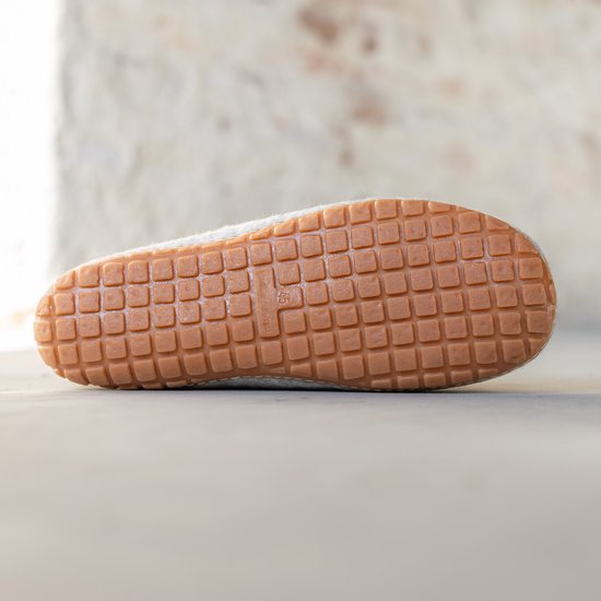 Onderkant van een lichtgrijze vilten pantoffel met bruine rubberen zool met vierkant profiel.