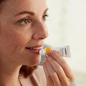 Een vrouw met sproeten brengt Purelan Lanolin cream op haar lippen aan vanuit een tube.