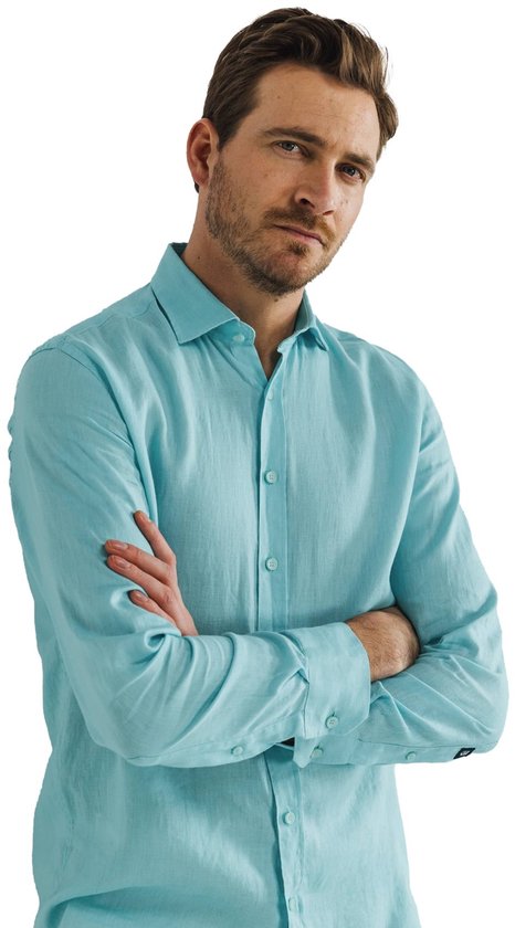 Man met armen over elkaar, draagt lichtblauwe linnen blouse. Zichtbare logo op de mouw.