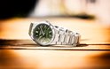 Edifice horloge met groene wijzerplaat en zilverkleurige metalen band, liggend op een houten ondergrond.
