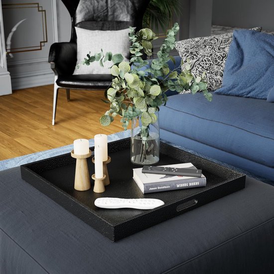 Zwart, lederen dienblad op een donkergrijs ottoman met een glazen vaas met eucalyptus, kaarsen en afstandsbedieningen.