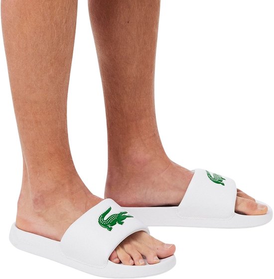 Witte Lacoste badslippers met groene krokodil op de band. Gedragen door een persoon.