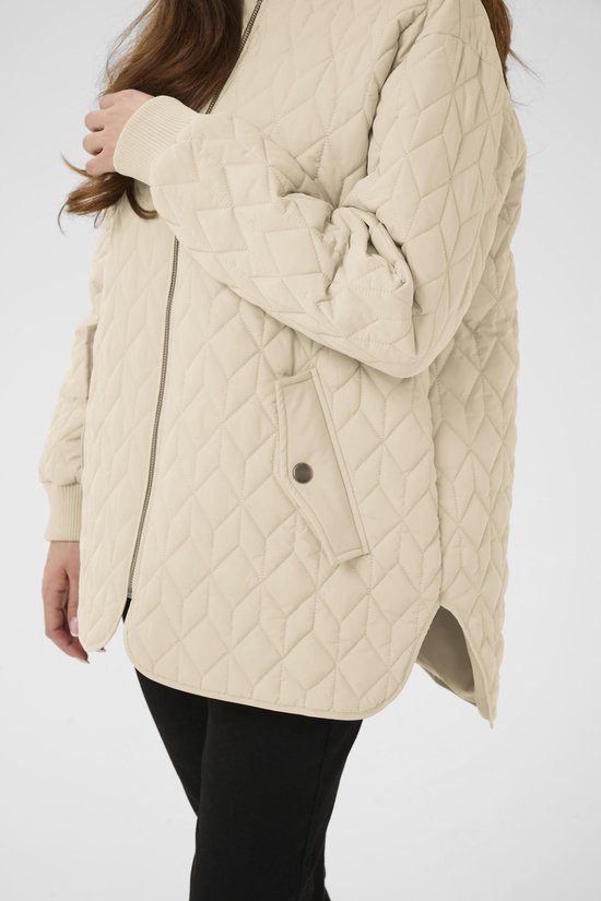 Detail van een beige gewatteerde jas met ruitpatroon, rits en drukknoopzak.