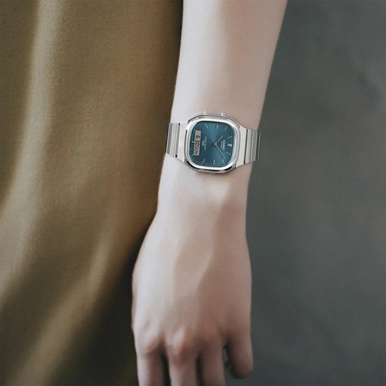 Casio-horloge met zilverkleurige stalen band en blauwe wijzerplaat, om een pols gedragen.