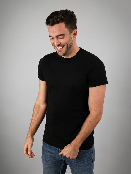 Een lachende man met een zwart Suitable T-shirt en blauwe jeans.