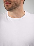 Close-up van de nek van een wit katoenen T-shirt met ronde hals en het SUITABLE merklabel.