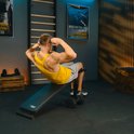 Man in geel sport-top doet buikspieroefening op de schuine trainingsbank.