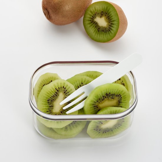 Boîte à lunch transparente remplie de tranches de kiwi, avec une fourchette blanche à l'intérieur.