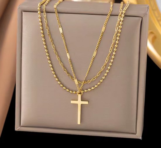 Gouden gelaagde ketting met kruishanger op een luxe bruine standaard.