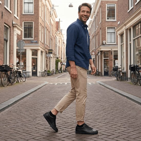 Man met donkerblauw overhemd en beige broek, zwarte sneakers en sokken, loopt door een straat.