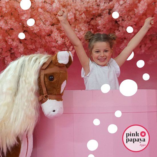 Meisje met armen omhoog in een roze setting, naast een bruin pluche paard.