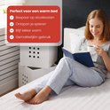 Vrouw in gestreept pyjama leest een boek en drinkt koffie op bed. Rode tekst: Perfect voor een warm bed.