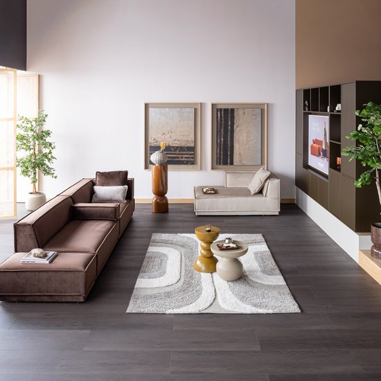 Ruim bruin hoekbankstel met chaise longue, bijzettafels, vloerkleed en kunst aan de muur.