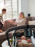 Zwarte ZAZU Baby Rocker aan een duwstang, met een baby in een kinderwagen en mensen op de achtergrond.