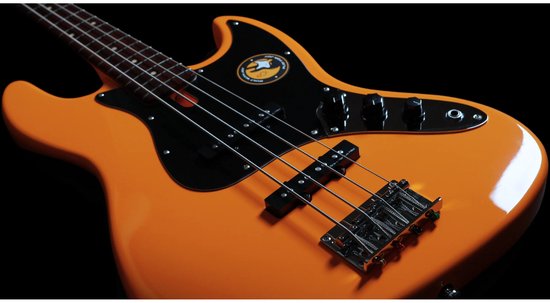 Close-up van een oranje elektrische basgitaar, met focus op de zwarte slagplaat en zilveren hardware.