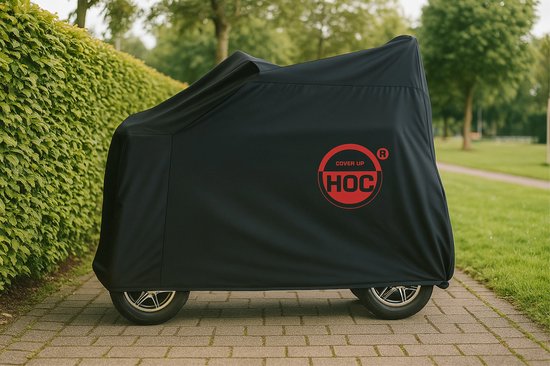 Zwarte scootmobielhoes op een betegeld pad, met rood 'COVER UP HOC' logo, in een groene omgeving.